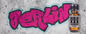 A graffiti-style text "berlin" in bold, pink letters is spray-painted on a gray, textured wall. Next to it, there is a small bottle labeled "berlin xxx hardcore" with a black cap and orange liquid inside. The urban artwork adds an edgy touch that makes this space feel like home.